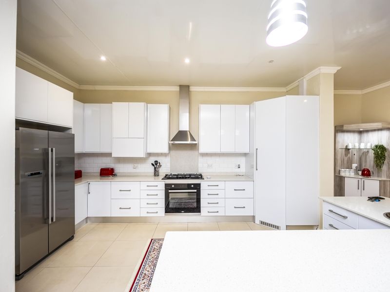 Modern kitchen featuring white high-gloss cabinetry, stone countertops, a central island, and integrated stainless steel appliances with a subway tile backsplash.