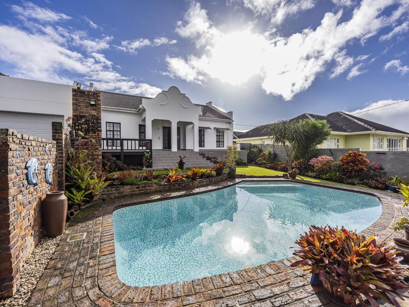A well-maintained backyard featuring a swimming pool with brick surround, raised patio area, and established garden landscaping.