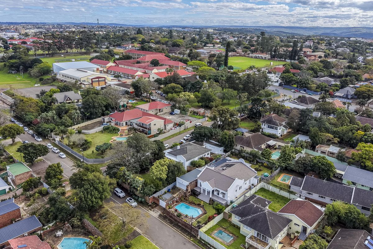An aerial view of a residential neighborhood featuring multiple homes with swimming pools, tiled roofs, and established gardens in a suburban setting.