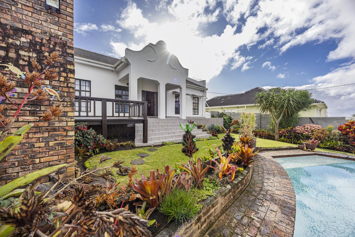 Rear view of the property featuring a swimming pool, brick-paved surround, raised timber deck, and well-maintained landscaped garden.