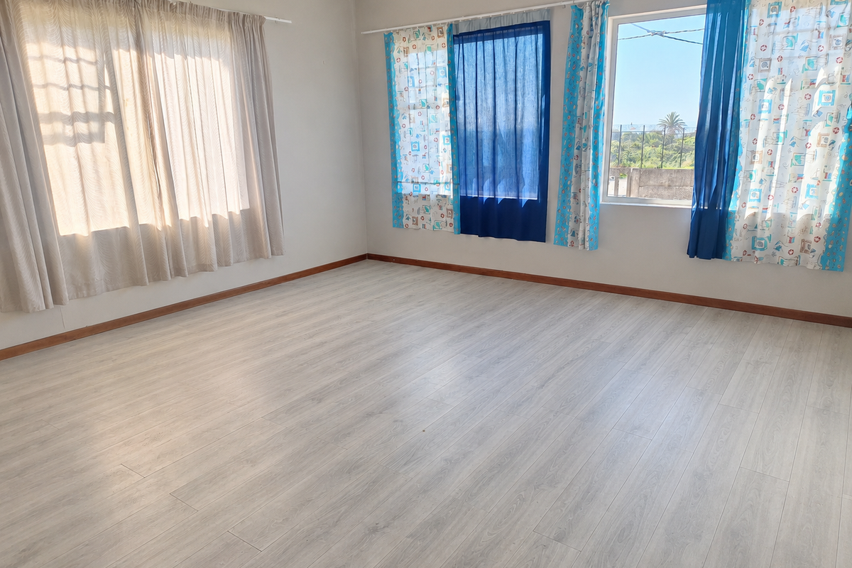 A bright and spacious empty bedroom featuring light-toned laminate flooring and large windows with natural light.