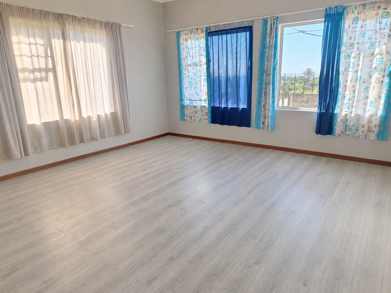 A bright and spacious empty bedroom featuring light-toned laminate flooring and large windows with natural light.