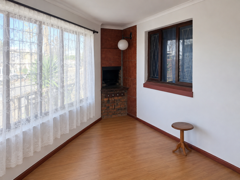 A bright living area featuring laminate flooring, a built-in corner fireplace with brick detailing, and large windows with natural light.
