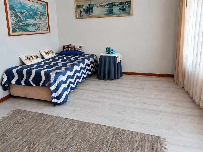 A well-maintained bedroom featuring light-toned laminate flooring and large windows with installed curtain tracks, offering a clean and neutral living space.