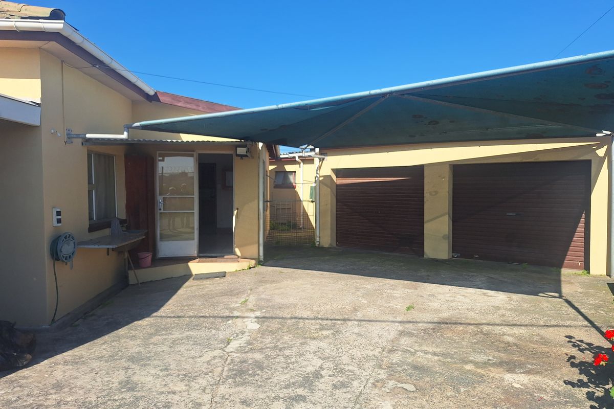 Rear exterior view featuring a double garage, concrete driveway, and a large shade sail covering the parking area.