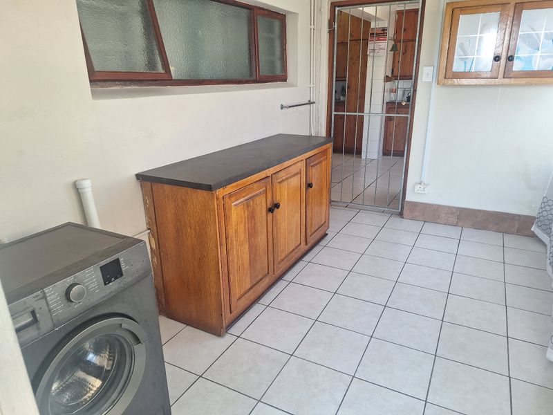 Functional laundry area featuring tiled flooring, built-in wooden cabinetry, and a secure access point leading to the kitchen.