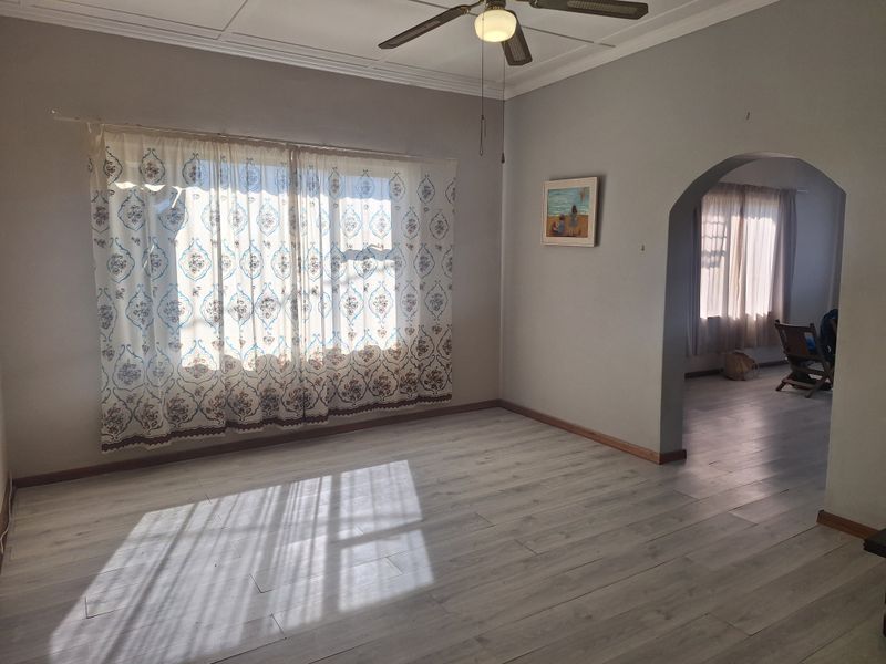 A bright and spacious living room featuring light-toned laminate flooring, a ceiling fan, and a classic arched entryway leading to an adjacent room.
