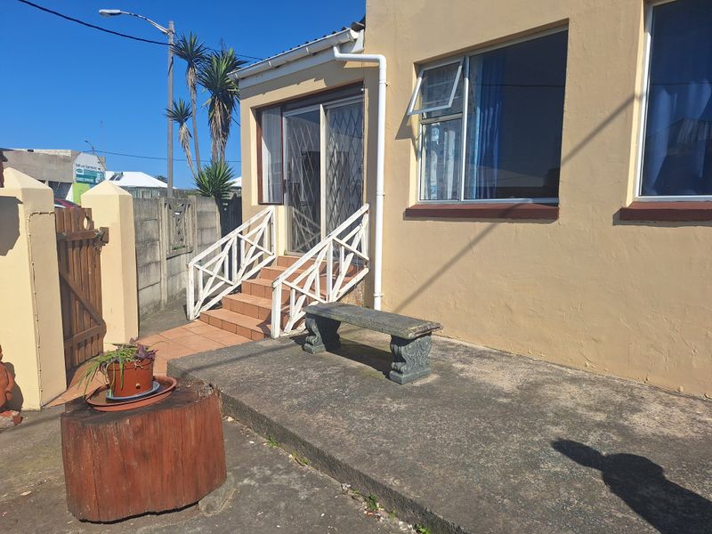 Front exterior view featuring a concrete patio, tiled entrance steps with railings, and a sliding security gate leading to the main entrance.