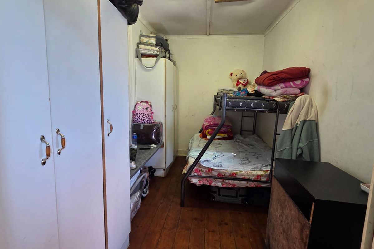 A compact bedroom featuring built-in cupboards and timber flooring, requiring some cosmetic updates to the wall finishes.