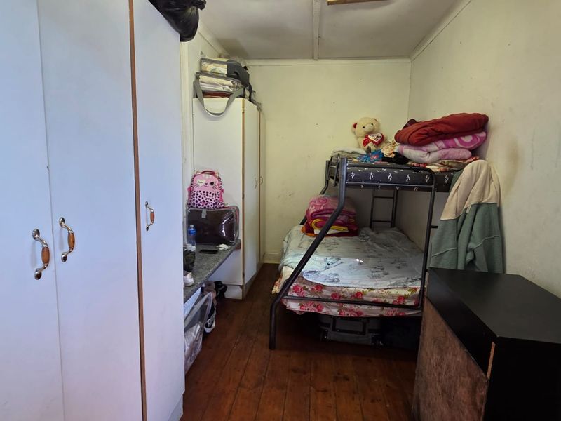 A compact bedroom featuring built-in cupboards and timber flooring, requiring some cosmetic updates to the wall finishes.