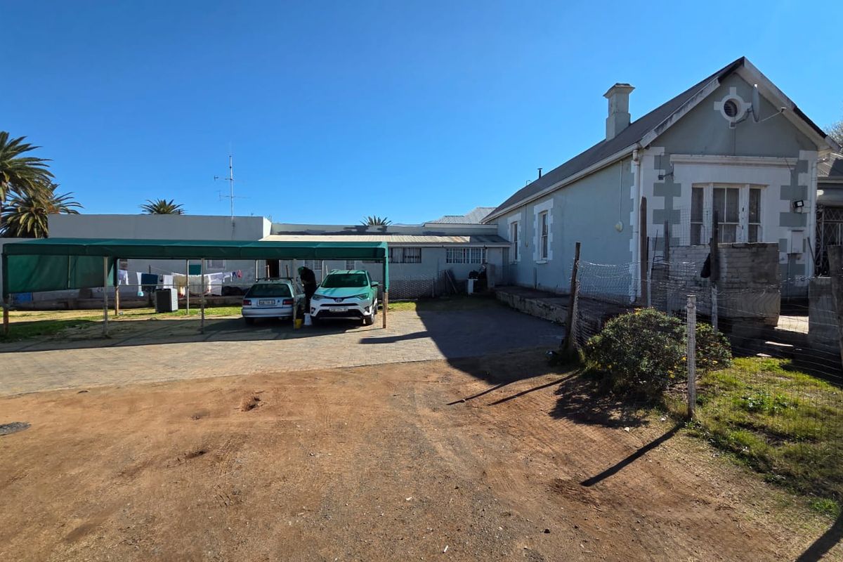 Rear exterior view of the property featuring a carport, paved driveway area, and existing perimeter fencing with visible wear to the building facade.