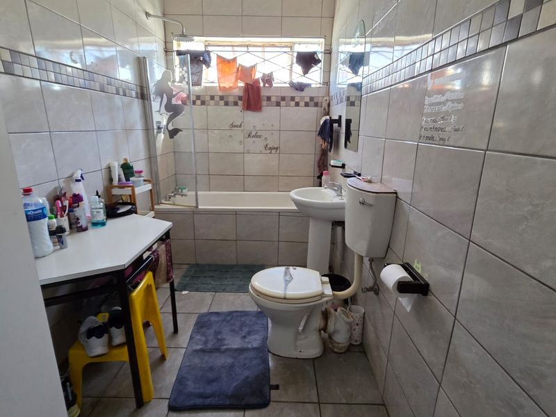A functional bathroom featuring a bathtub with shower head, pedestal basin, and toilet, finished with neutral ceramic wall and floor tiles.