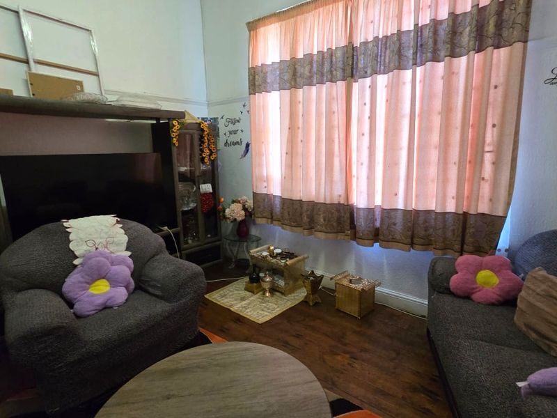 A living room featuring laminate flooring and a large window with curtains, providing a functional space for relaxation.