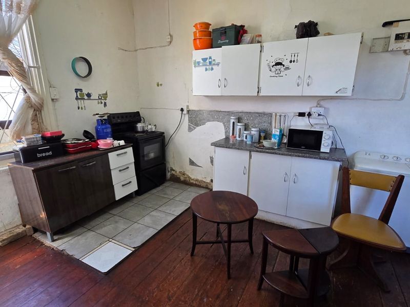 A dated kitchen area featuring built-in cabinetry, a stove, and a mix of timber and tiled flooring, currently requiring significant maintenance and cosmetic updates.