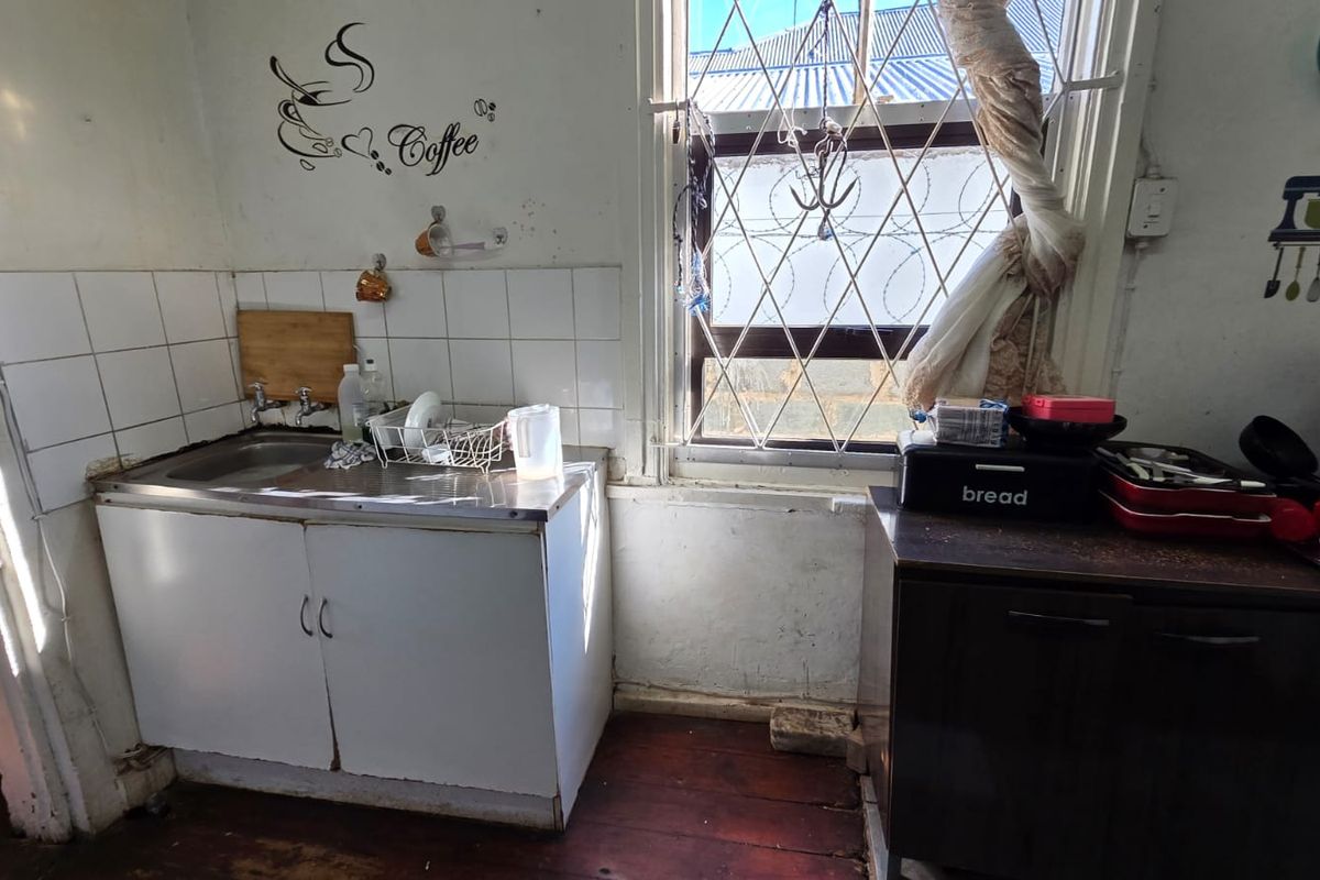 A compact kitchen area featuring a stainless steel sink, tiled splashback, and built-in cabinetry, requiring cosmetic updates to improve its overall condition.