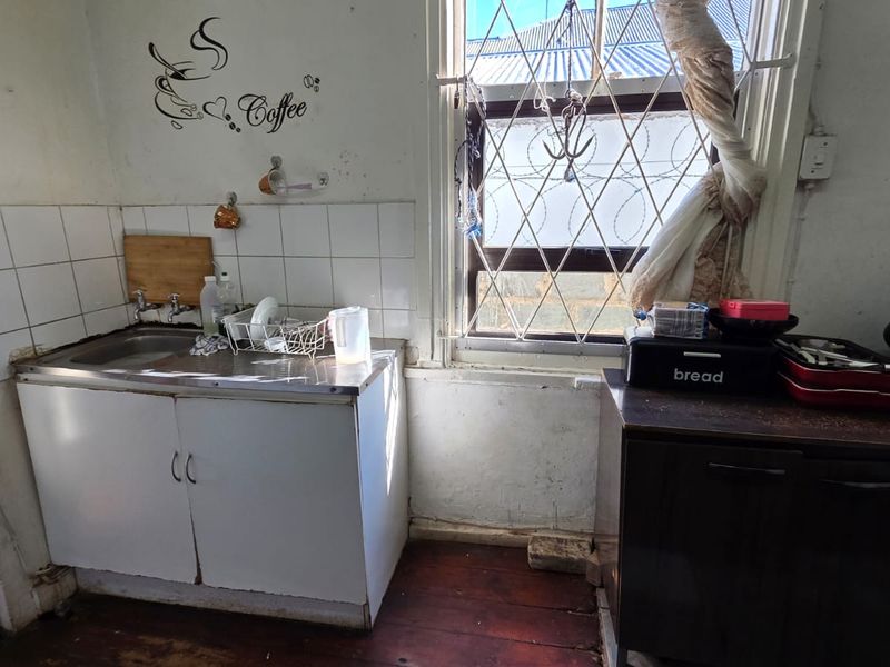 A compact kitchen area featuring a stainless steel sink, tiled splashback, and built-in cabinetry, requiring cosmetic updates to improve its overall condition.