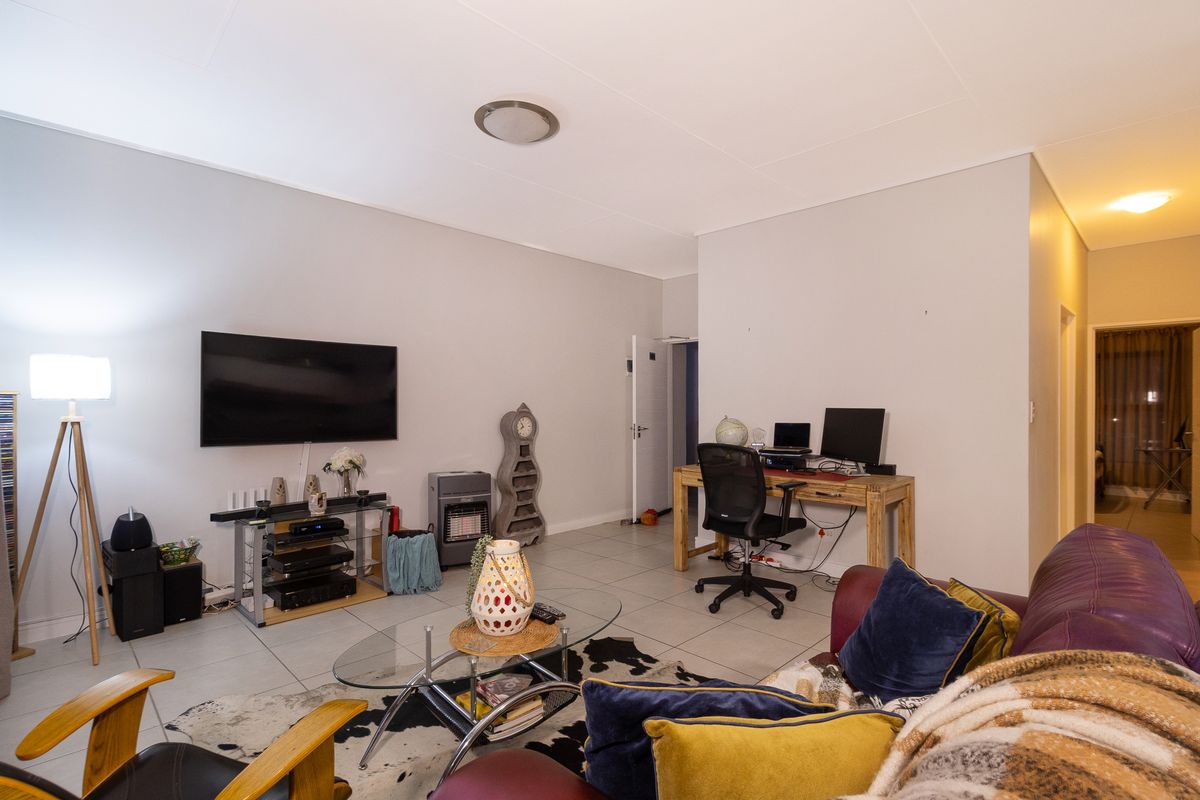 A spacious living area featuring neutral walls and tiled flooring, providing a versatile layout suitable for both relaxation and a home office setup.