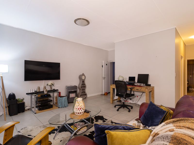 A spacious living area featuring neutral walls and tiled flooring, providing a versatile layout suitable for both relaxation and a home office setup.