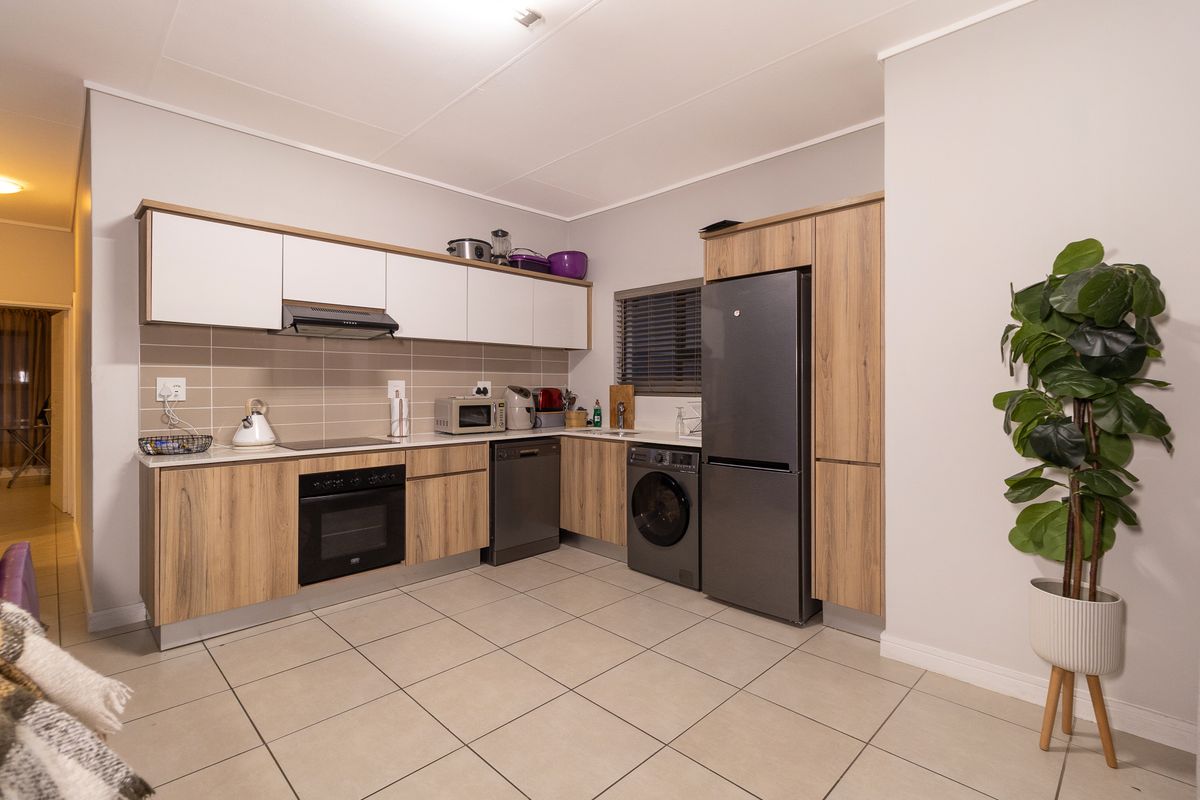 Modern kitchen featuring wood-grain and white cabinetry, tiled backsplash, integrated oven, extractor fan, and built-in laundry and dishwasher appliances.