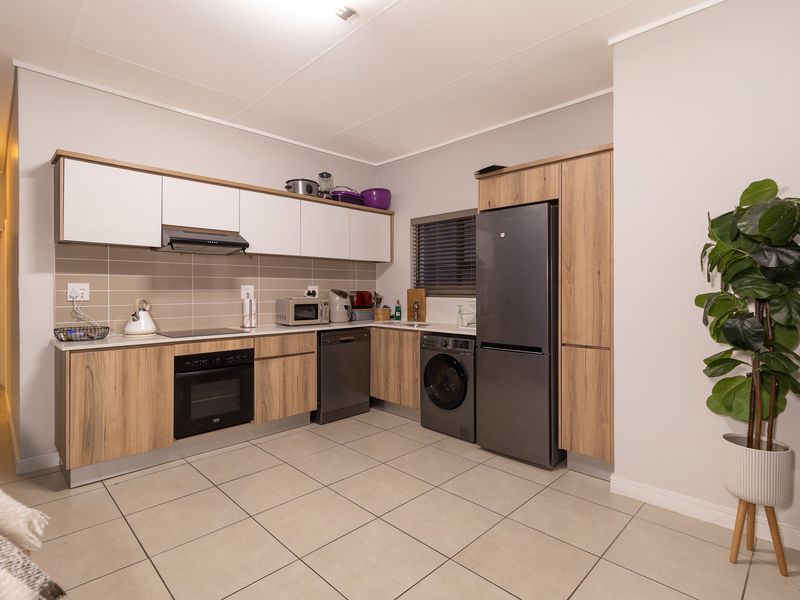 Modern kitchen featuring wood-grain and white cabinetry, tiled backsplash, integrated oven, extractor fan, and built-in laundry and dishwasher appliances.