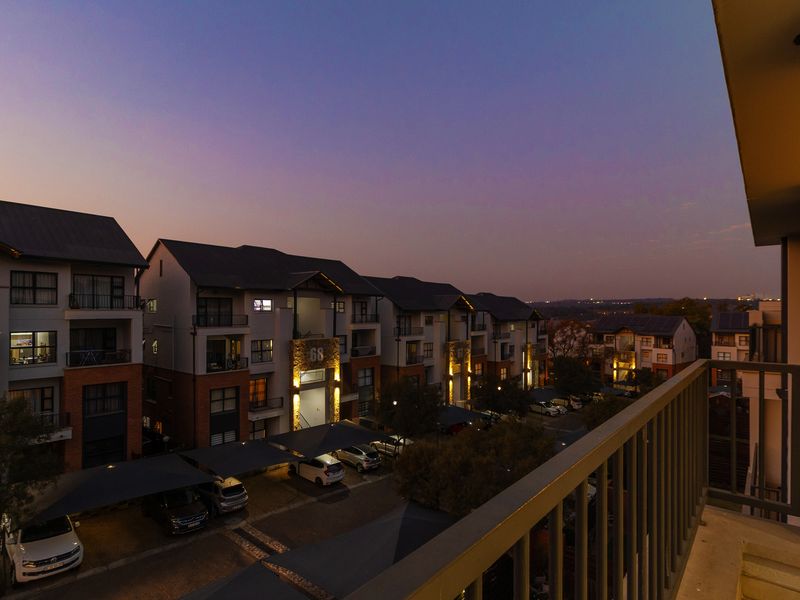 Elevated view from a balcony overlooking the apartment complex grounds, covered parking areas, and surrounding neighborhood at dusk.