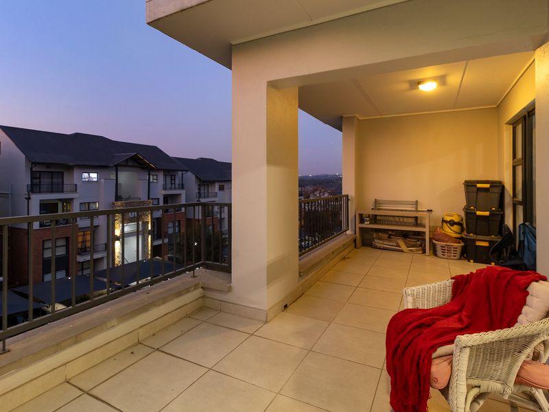 A covered balcony featuring tiled flooring and a metal balustrade, offering an elevated view of the surrounding apartment complex at dusk.