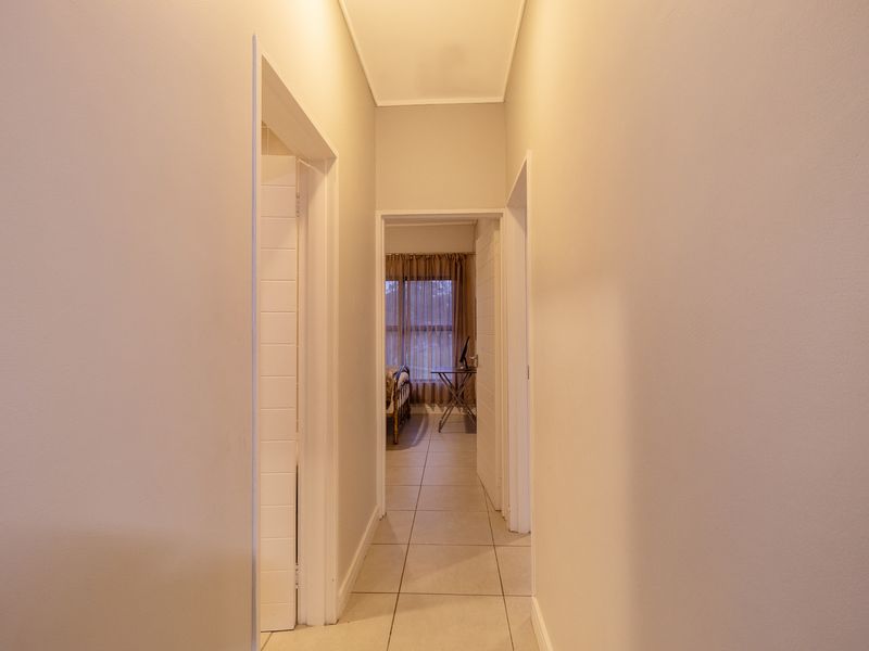 A clean, well-lit hallway with neutral walls and tiled flooring, providing access to adjacent rooms within the apartment.