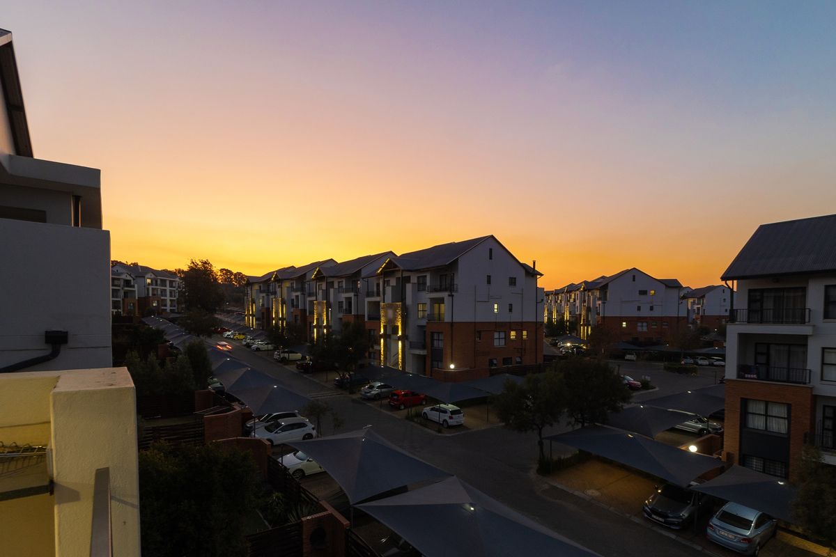 An elevated aerial view of a modern apartment complex at sunset, featuring paved parking areas with shade cloth carports and multi-story residential buildings.