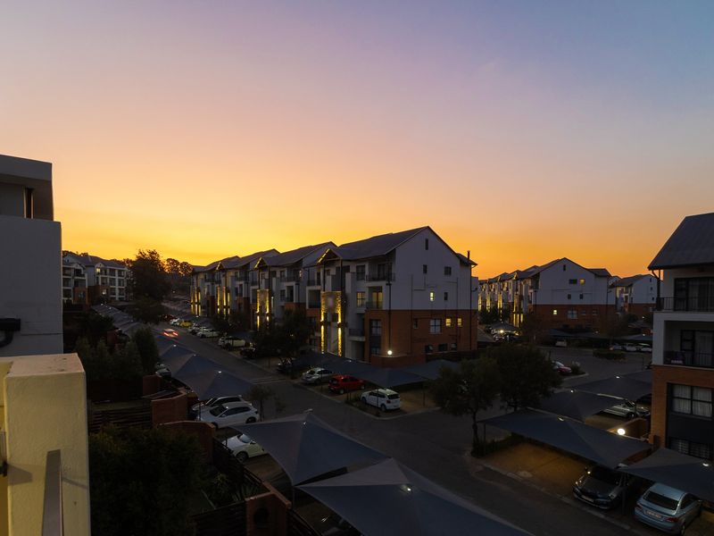 An elevated aerial view of a modern apartment complex at sunset, featuring paved parking areas with shade cloth carports and multi-story residential buildings.
