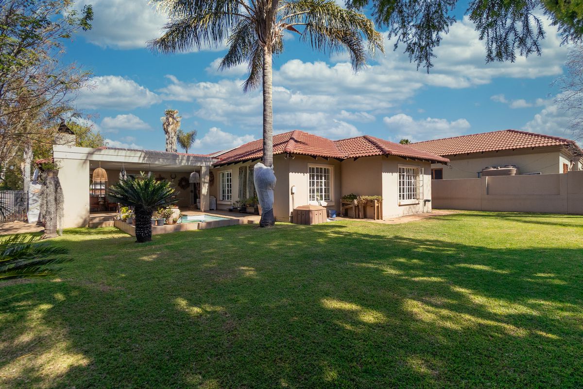 Rear view of the house featuring a spacious lawn, a covered patio area, and a swimming pool set within a private garden.