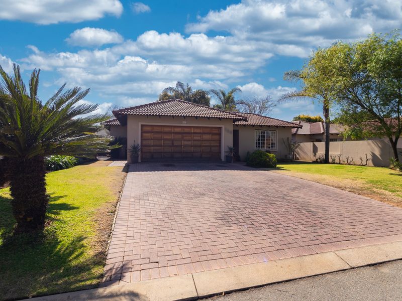 Front view of a single-story house featuring a paved driveway, a tiled roof, and a well-maintained garden.