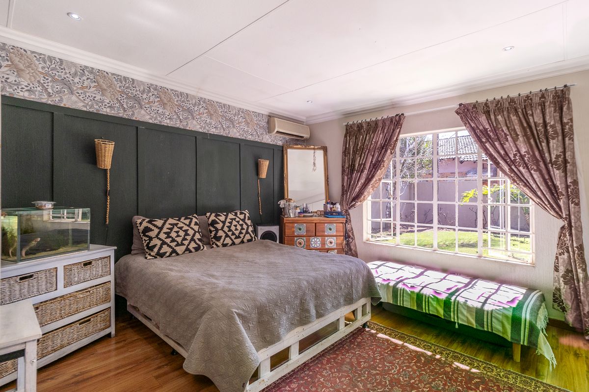 A well-lit bedroom featuring dark decorative wall paneling, patterned wallpaper, laminate flooring, and a large window overlooking the garden.