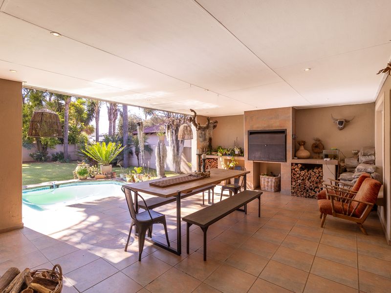 Spacious covered patio featuring a built-in braai, tiled flooring, and recessed lighting, overlooking a private swimming pool and garden area.