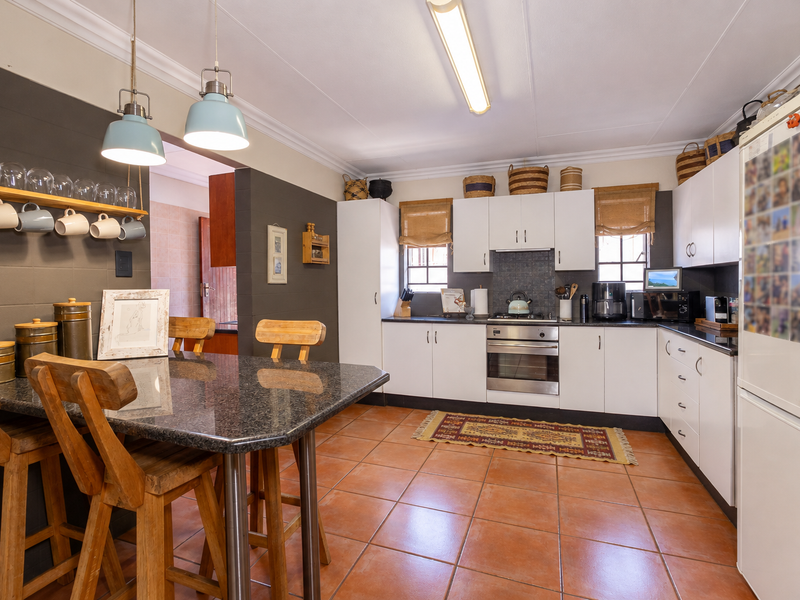 A functional kitchen featuring white cabinetry, granite countertops, integrated stainless steel appliances, and terracotta floor tiles with a breakfast nook area.