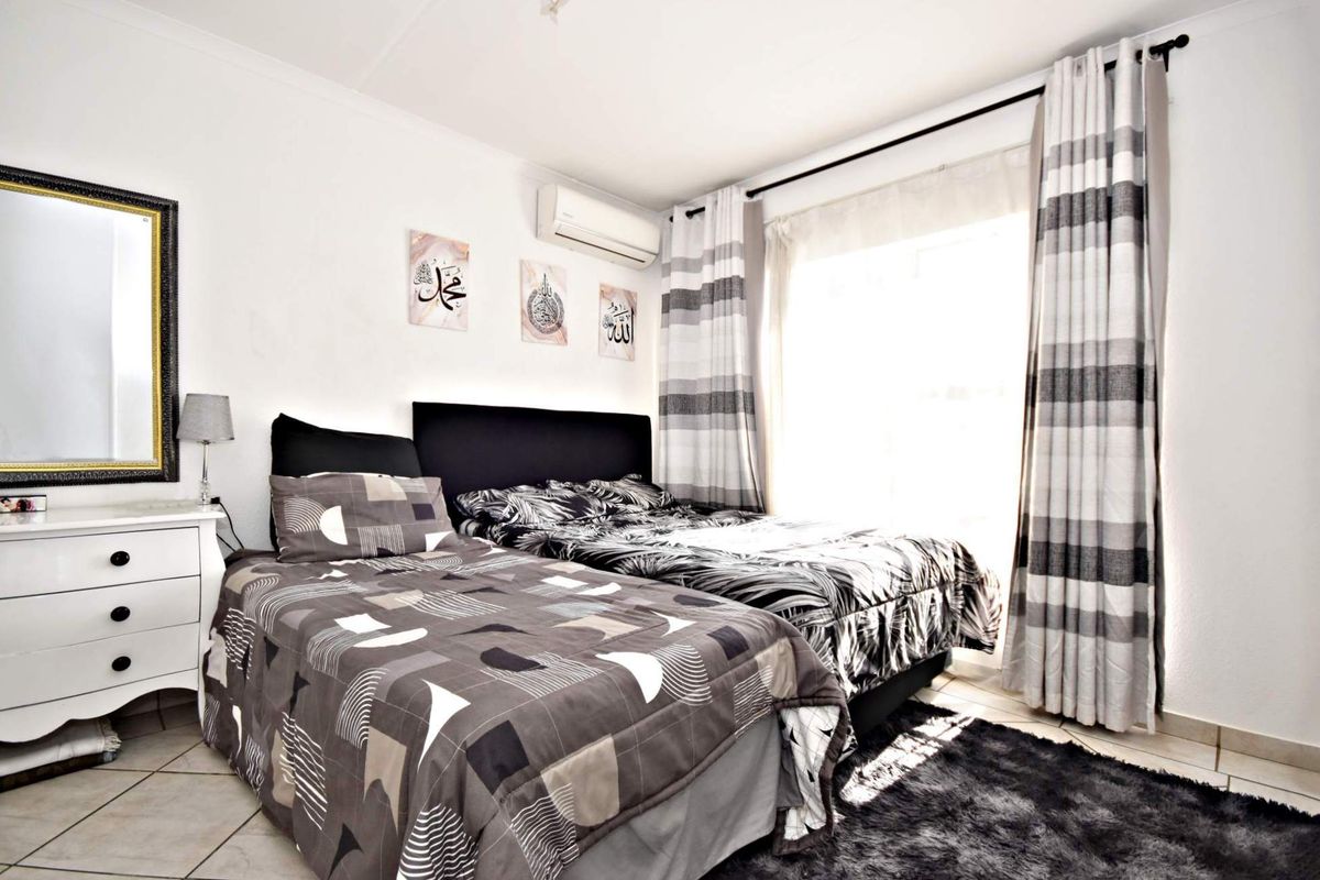 A well-maintained bedroom featuring tiled flooring, a wall-mounted split-system air conditioner, and large windows with fitted curtain tracks.