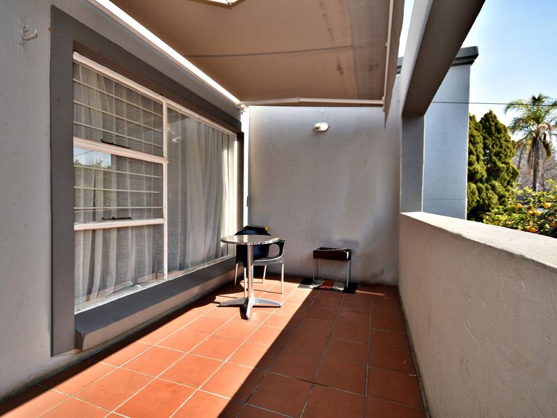 A private balcony featuring tiled flooring, a retractable awning for shade, and security bars on the window, offering a functional outdoor space.