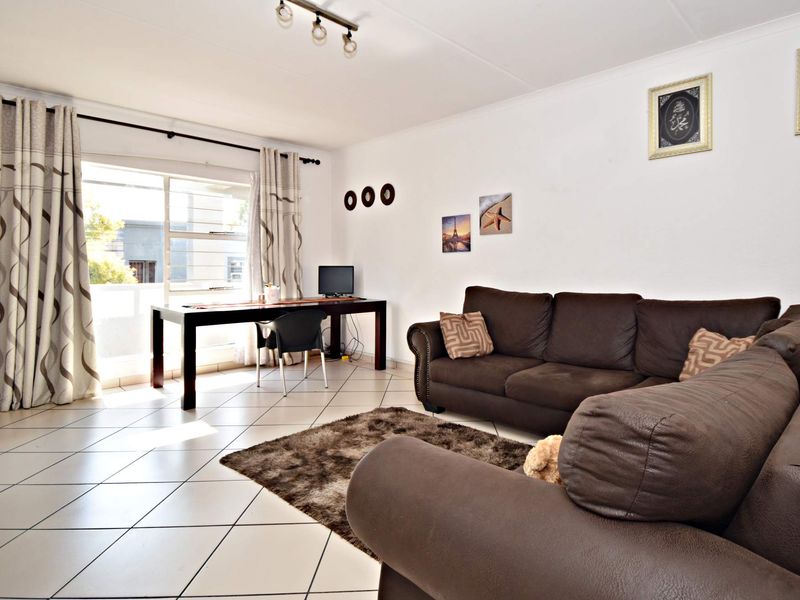 A bright living room featuring tiled flooring, track lighting, and a large sliding glass door providing access to the balcony.