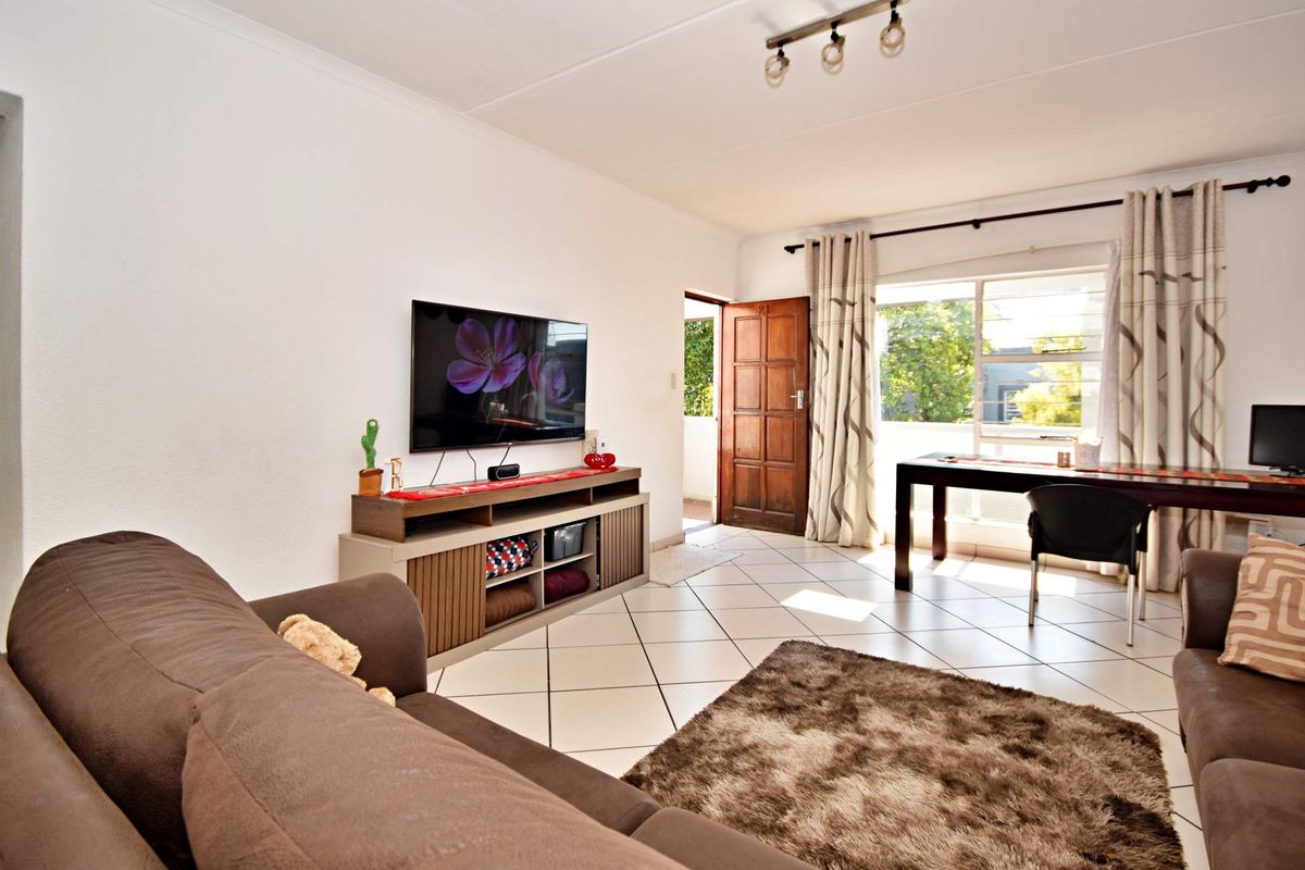 A bright living room featuring tiled flooring, track lighting, and direct access to an outdoor area through a timber door.