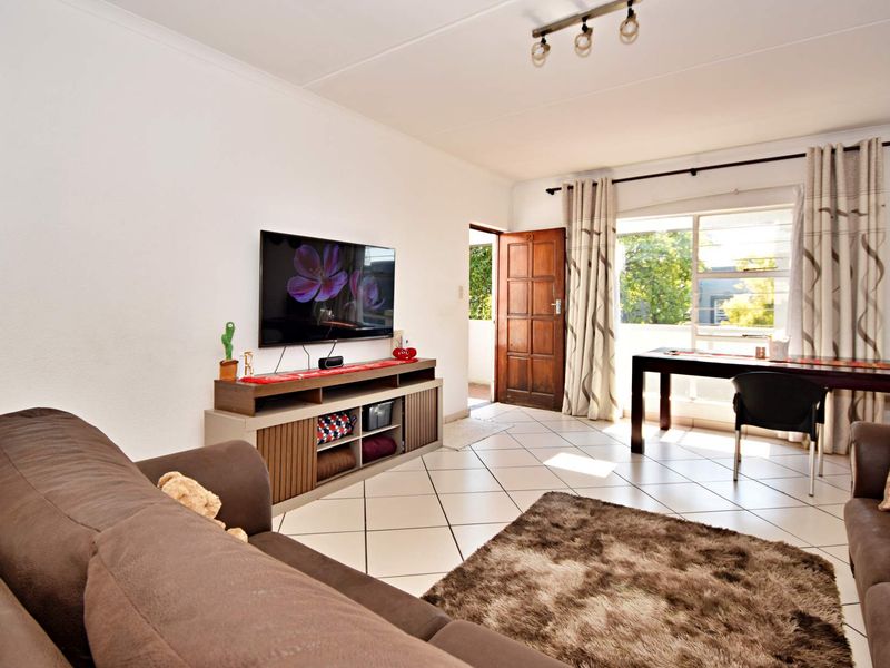 A bright living room featuring tiled flooring, track lighting, and direct access to an outdoor area through a timber door.