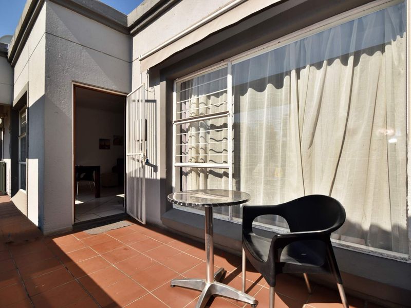 A private balcony area featuring tiled flooring, a security gate, and large windows providing access to the interior living space.