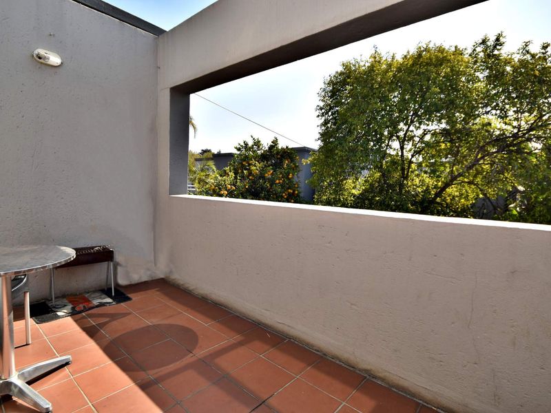 A private balcony featuring terracotta floor tiles and a concrete parapet wall, offering an open outlook with mature greenery.