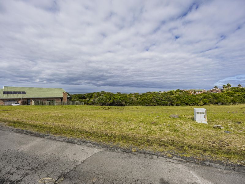 A vacant residential plot featuring a grassed surface, an electrical distribution box, and direct access to a paved road.