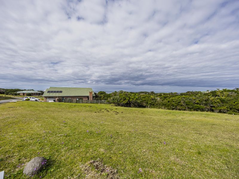 A wide-angle view of a residential vacant land plot featuring a grassy lawn with a neighboring house and solar panels visible in the background.