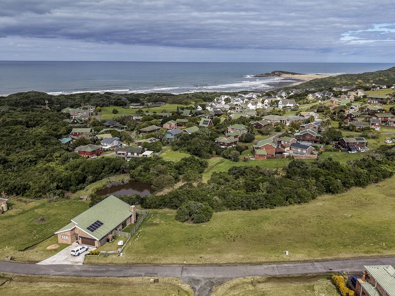 An aerial view of a coastal residential estate featuring green landscapes, natural vegetation, and proximity to the ocean.