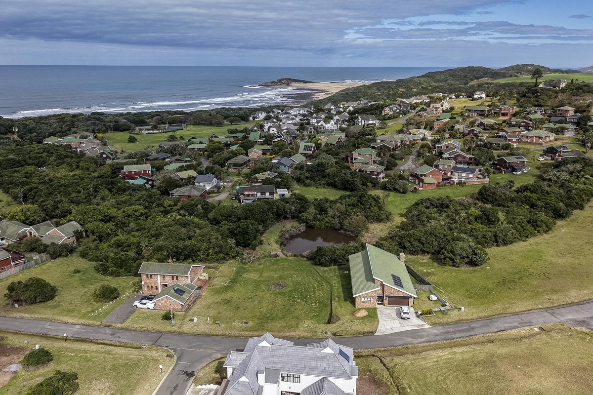 An aerial view of a coastal residential estate featuring paved roads, established greenery, and proximity to the ocean.