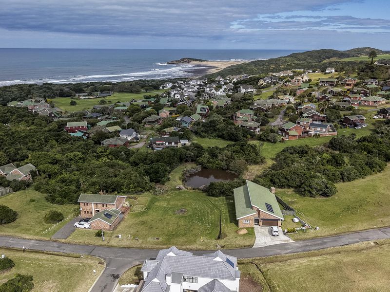 An aerial view of a coastal residential estate featuring paved roads, established greenery, and proximity to the ocean.