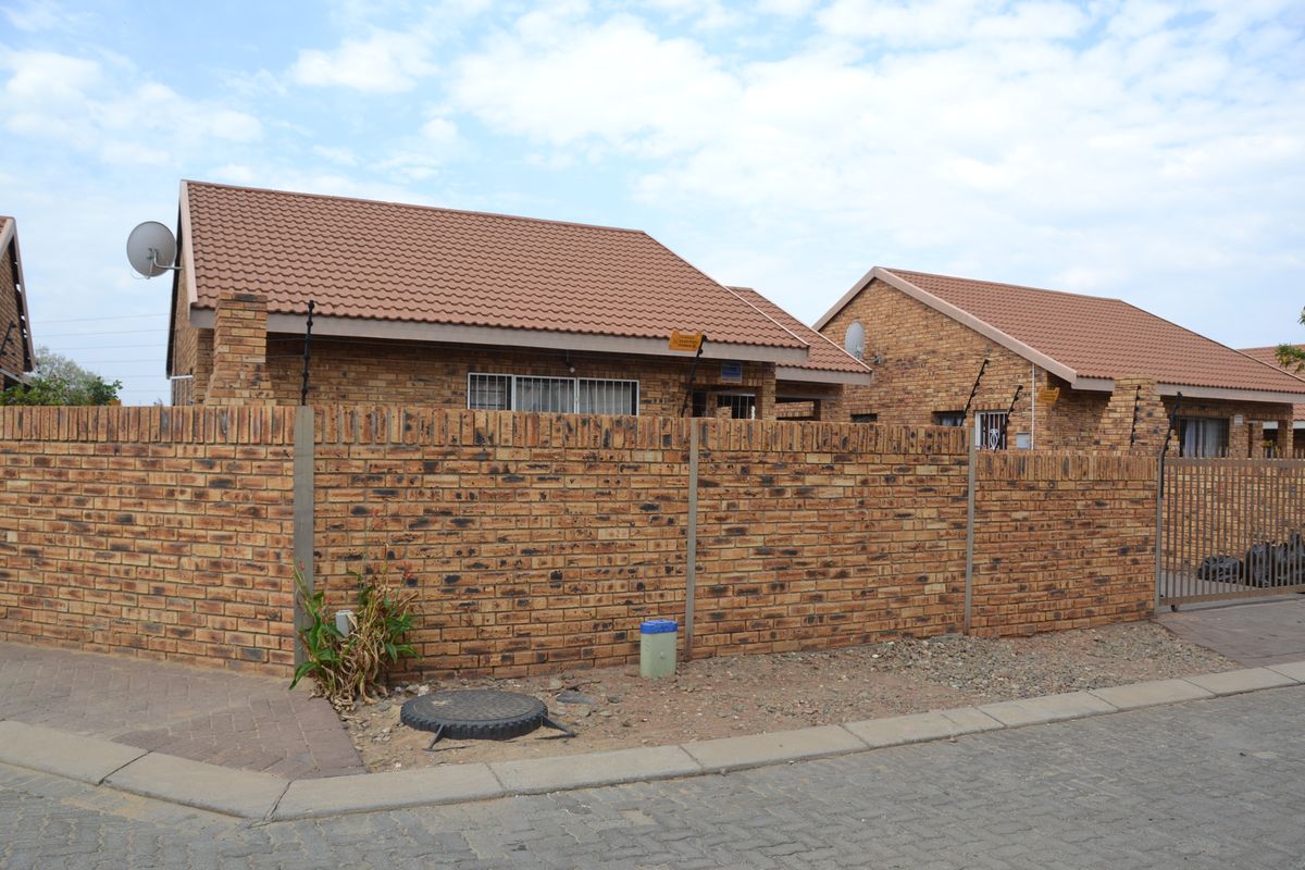 Front view of a face brick residential house featuring a tiled roof, secure perimeter wall with electric fencing, and a paved driveway entrance.