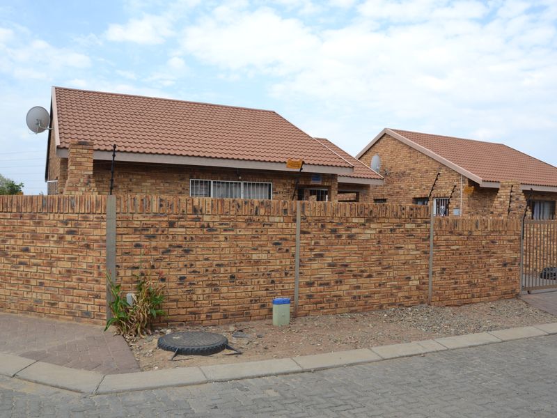 Front view of a face brick residential house featuring a tiled roof, secure perimeter wall with electric fencing, and a paved driveway entrance.