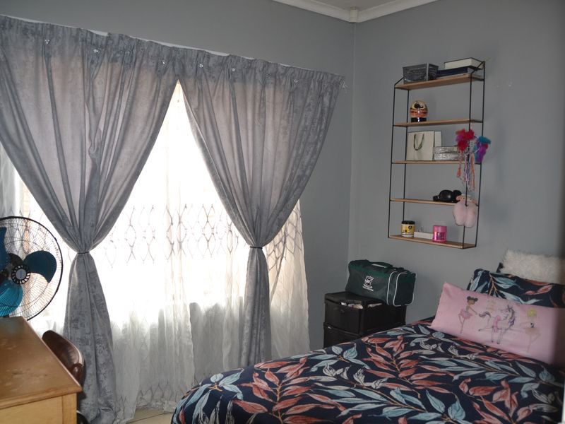 A functional bedroom featuring a window with security gate and curtain rails, finished with neutral wall paint.
