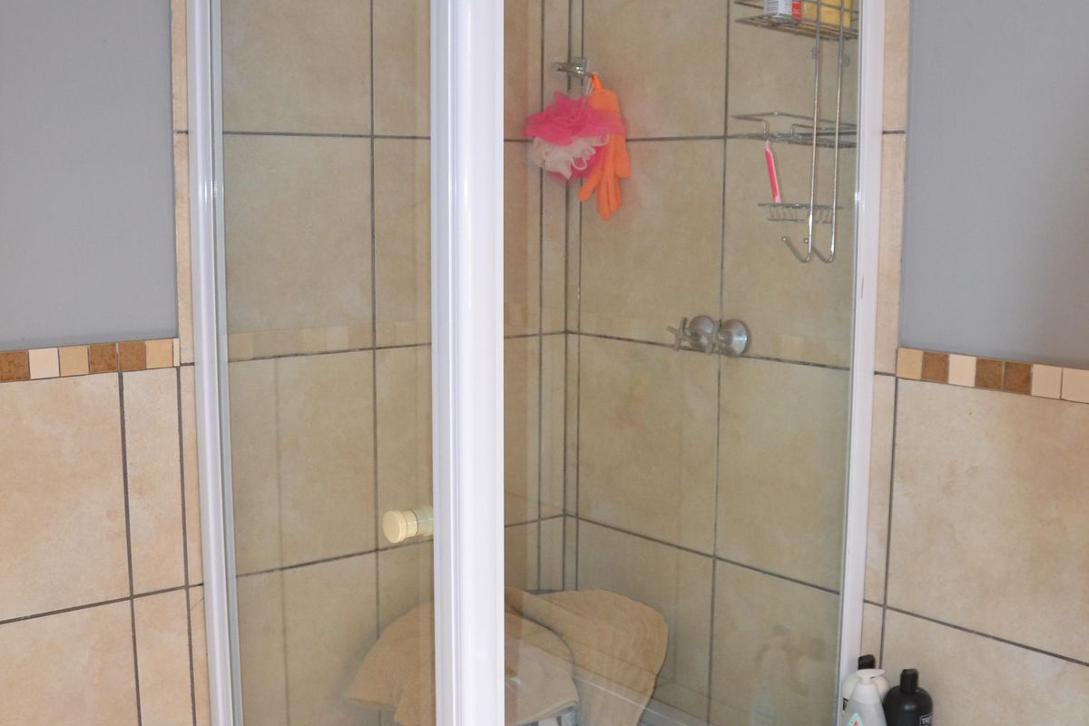 A bathroom featuring a corner shower enclosure with white framing, tiled walls and flooring, and a built-in bathtub.